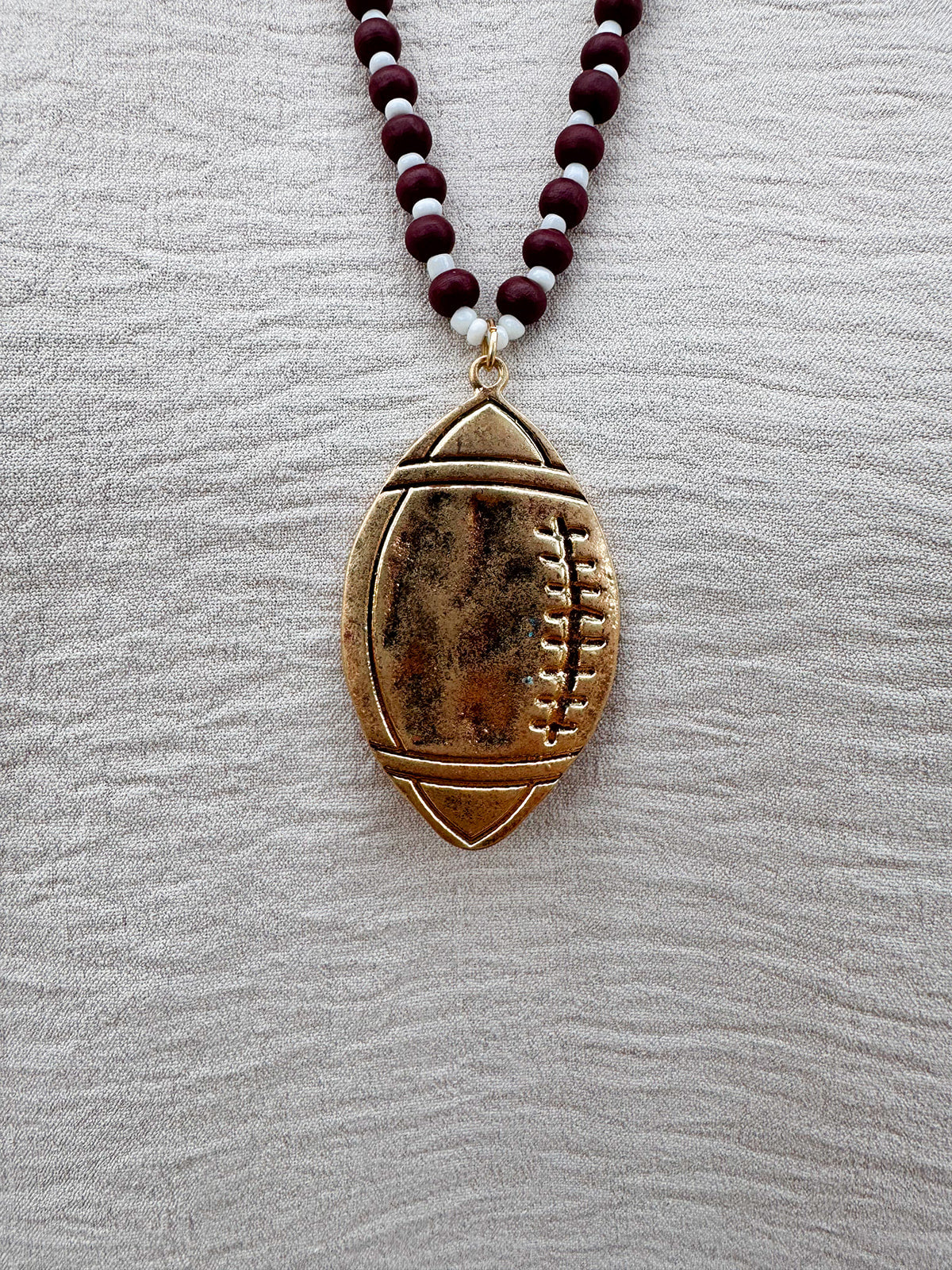 Long beaded necklace with alternating garnet and white beads, featuring a gold football pendant. A bold yet fun Gameday accessory.