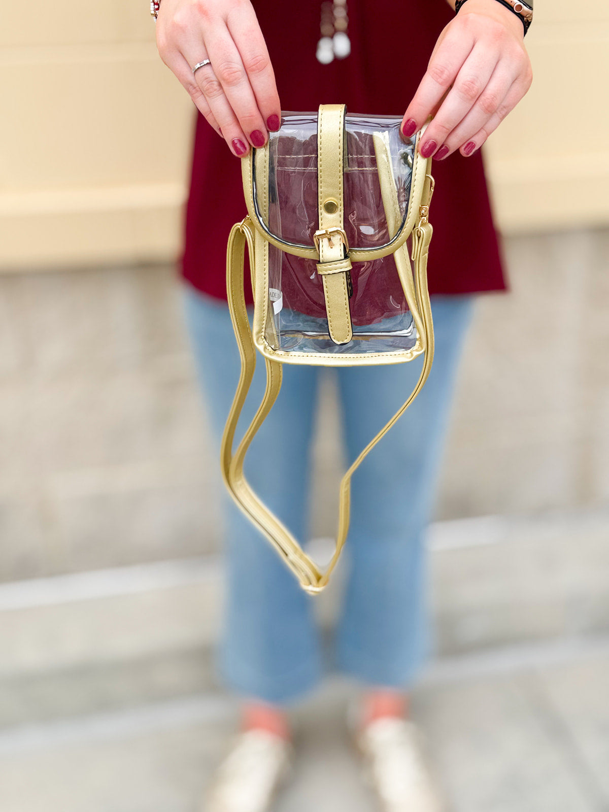 Clear crossbody bag with gold faux leather trim and belt buckle accent, perfect for stadium entry.