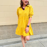 Mustard cotton mini dress with a collar, tiered A-line shape, and smocked cuff balloon sleeves—perfect for gameday style.