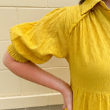 Mustard cotton mini dress with a collar, tiered A-line shape, and smocked cuff balloon sleeves—perfect for gameday style.