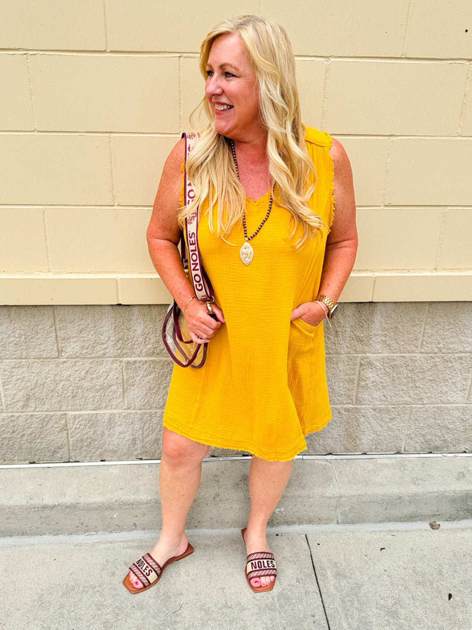 Sleeveless mustard cotton gauze dress with V-neckline, raw frayed edges, and front pockets. Lightweight and casual—ideal for Gameday or fall outings.