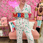 White pajama set with pink and green holiday house print, button-down top, and drawstring pants.