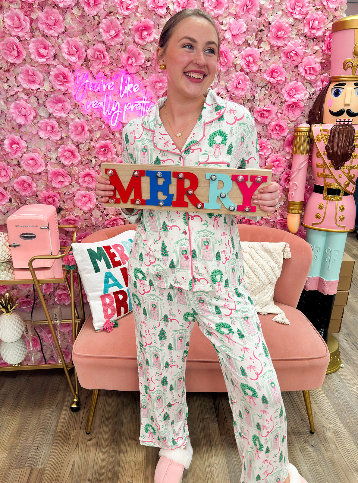 White pajama set with pink and green holiday house print, button-down top, and drawstring pants.