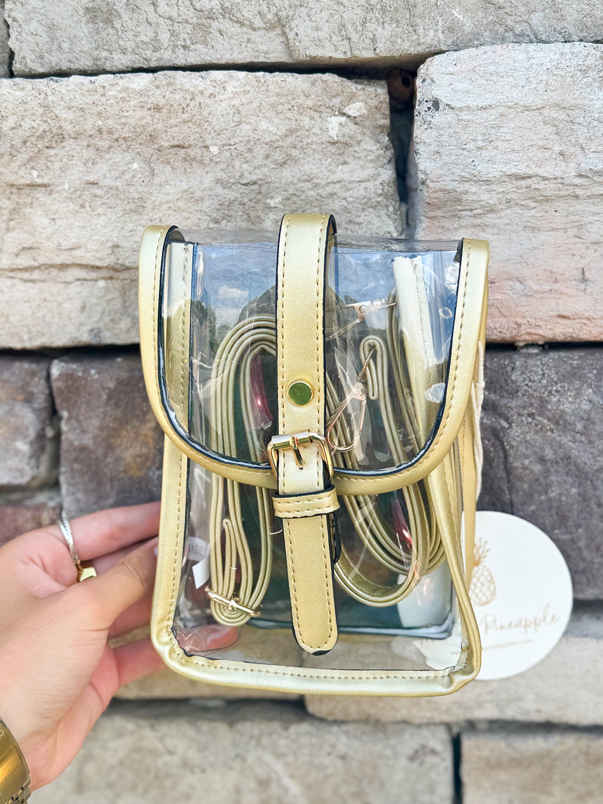 Clear crossbody bag with gold faux leather trim and belt buckle accent, perfect for stadium entry.