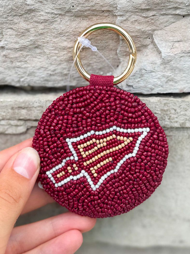 Maroon keychain with a logo held by a hand against a stone background