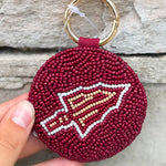 Maroon keychain with a logo held by a hand against a stone background