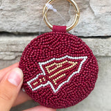 Maroon keychain with a logo held by a hand against a stone background