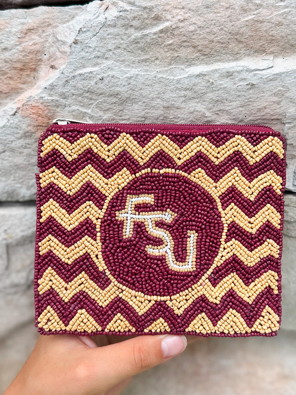Maroon and gold chevron patterned pouch with 'FSU' logo held against a stone background