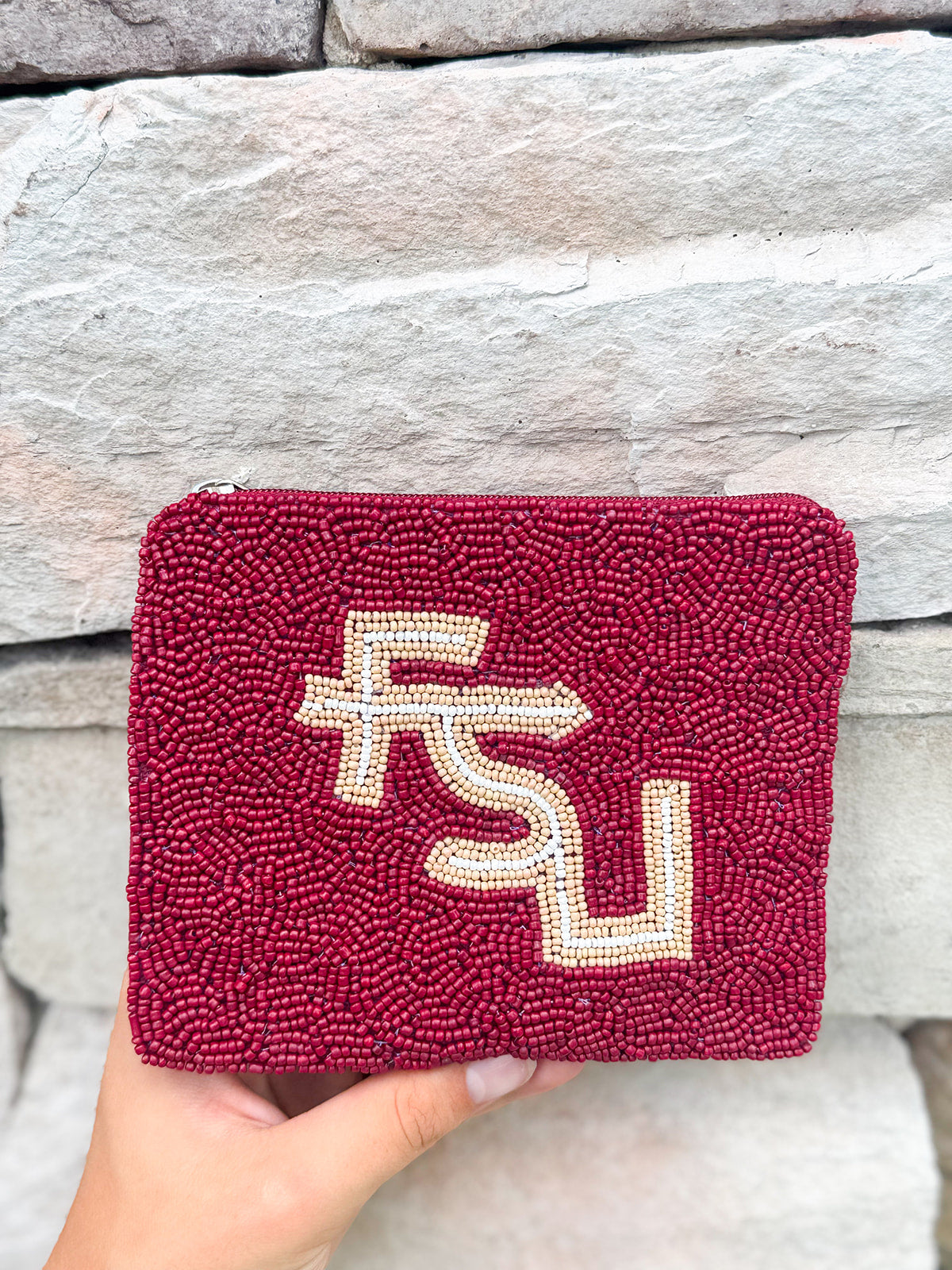 Maroon beaded clutch with FSU logo held against a stone wall.