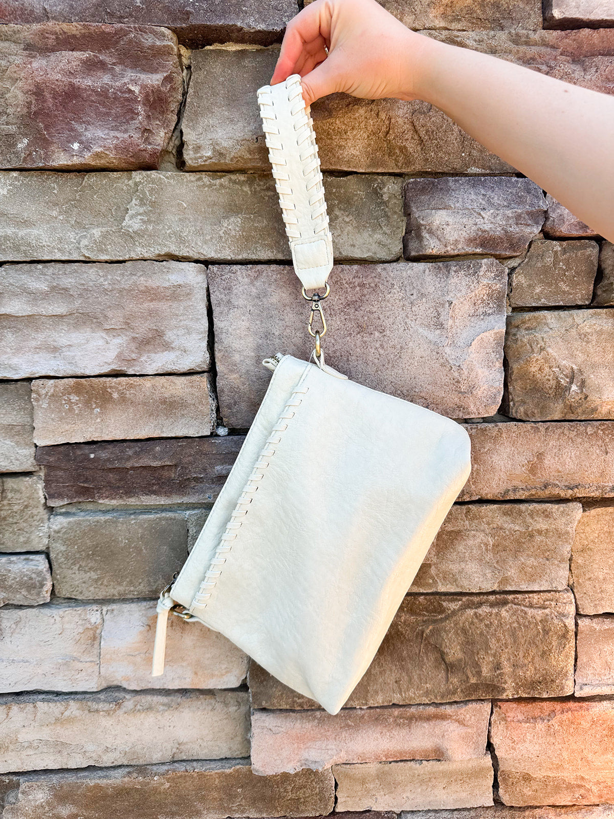 Joy Susan Gigi Crossbody Bag in Cotton shown with antiqued vegan leather, woven wrist strap, and gold-tone hardware – styled as a versatile accessory worn as a clutch, wristlet, or crossbody.