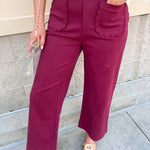 Burgundy straight-leg ankle pants with scalloped front pockets and a structured woven fabric with a denim-inspired finish.