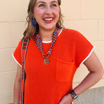 Orange short sleeve sweater knit top with cream contrast trim, crew neckline, and front chest pocket.