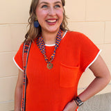 Orange short sleeve sweater knit top with cream contrast trim, crew neckline, and front chest pocket.