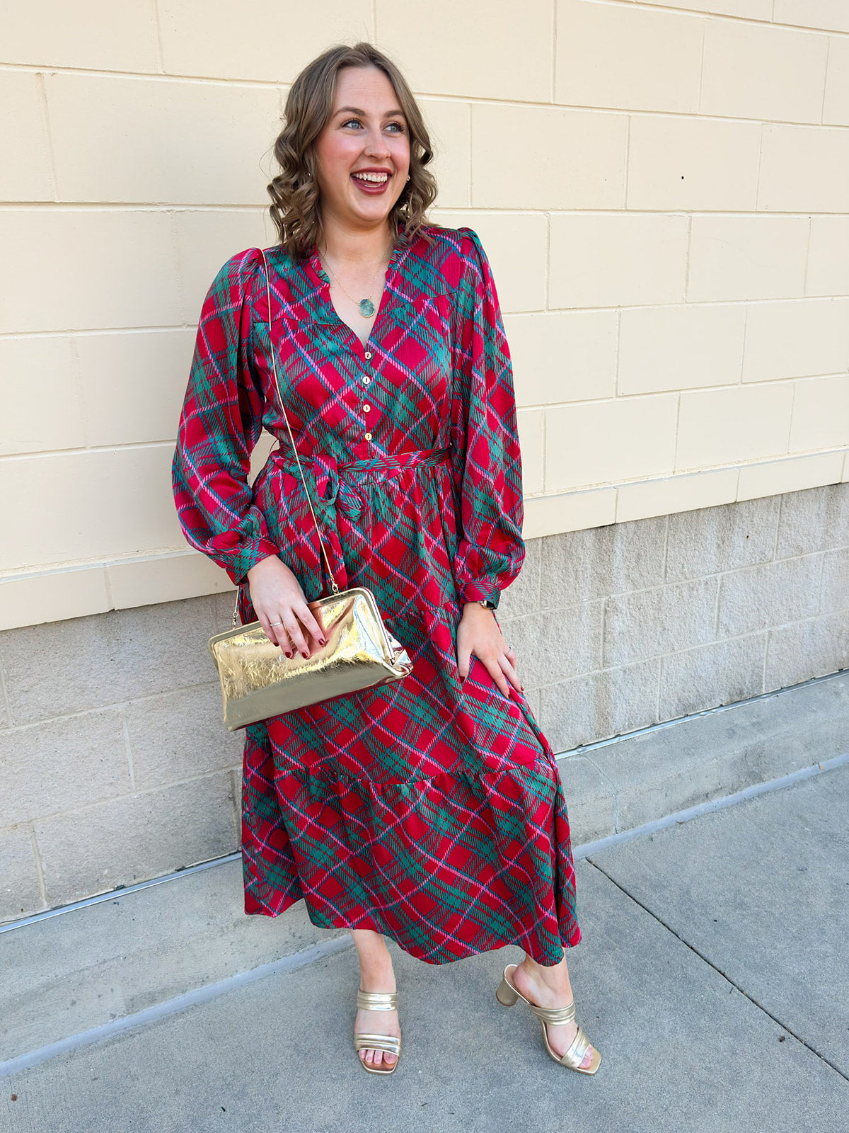 A pink, red, and green plaid tiered midi dress with ruffle neckline and long sleeves.