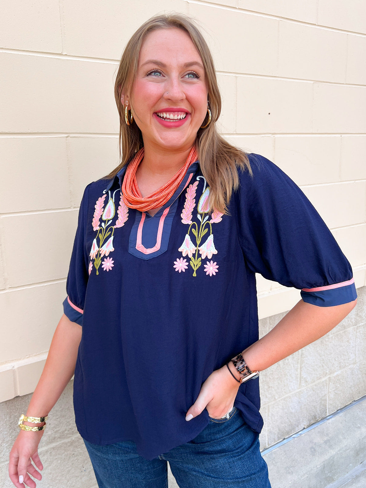 Navy flowy blouse with collared V-neckline, floral details, and short puff sleeves with cuffed hems.