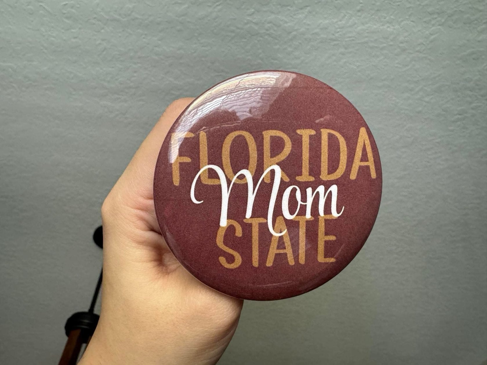 A garnet, gold, and white Florida State Mom pin attached to a neutral bag, perfect for FSU game day.