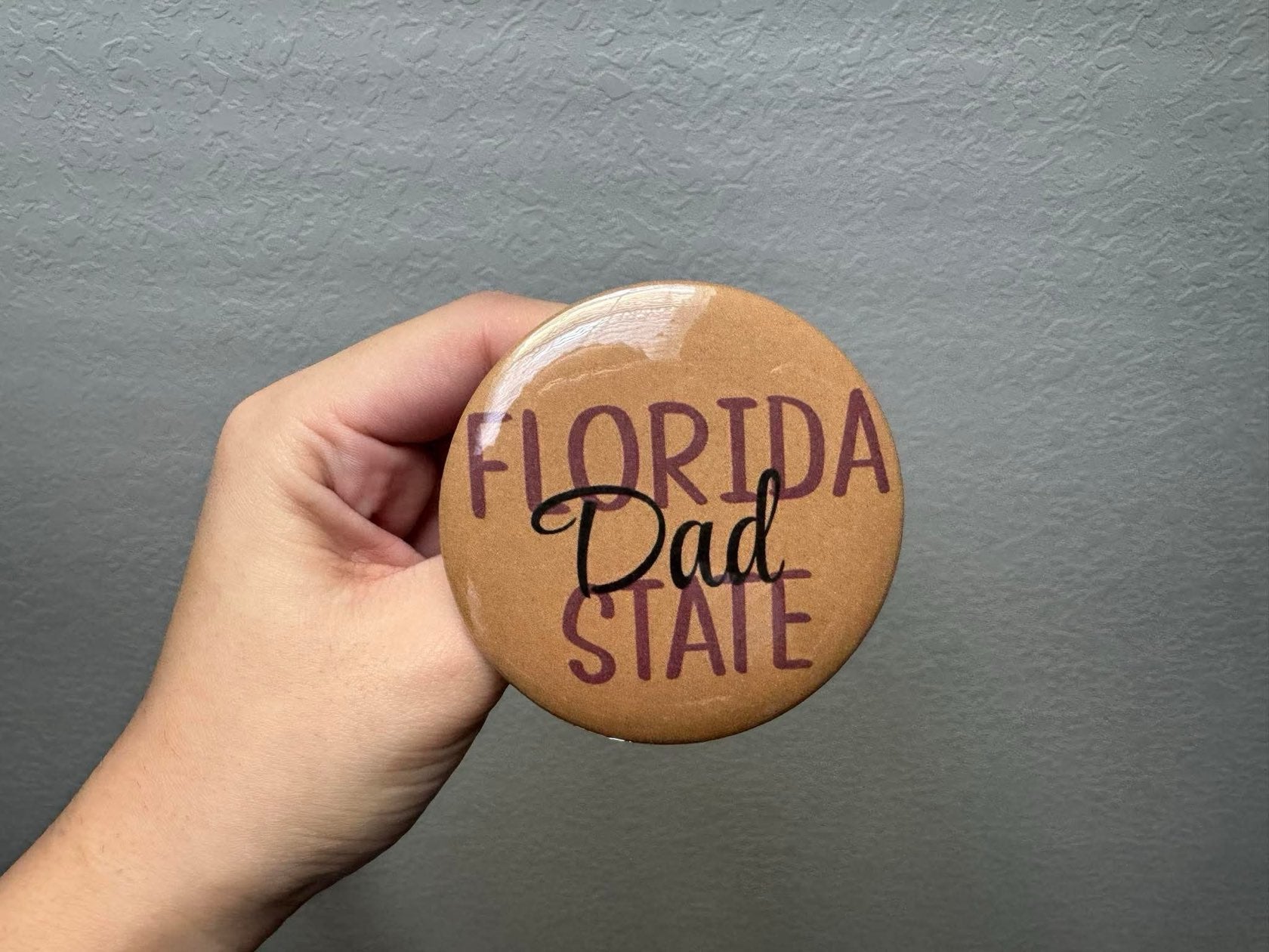 A garnet, gold, and black Florida State Dad pin attached to a neutral bag, perfect for FSU game day.