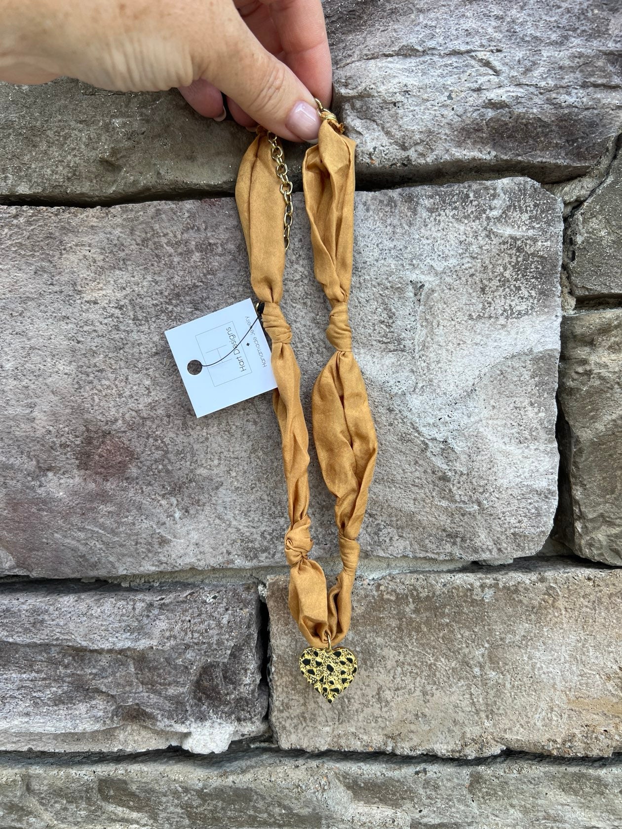 Gold scarf-style necklace with knotted details and hammered metal heart pendant.