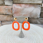 Gold stud drop earrings featuring orange oval hoops with smaller white rattan oval hoops layered inside