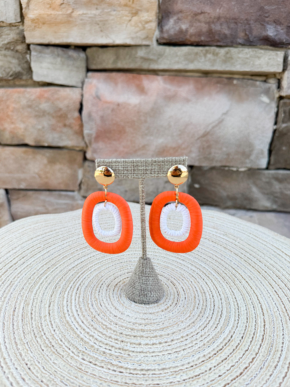 Gold stud drop earrings featuring orange oval hoops with smaller white rattan oval hoops layered inside