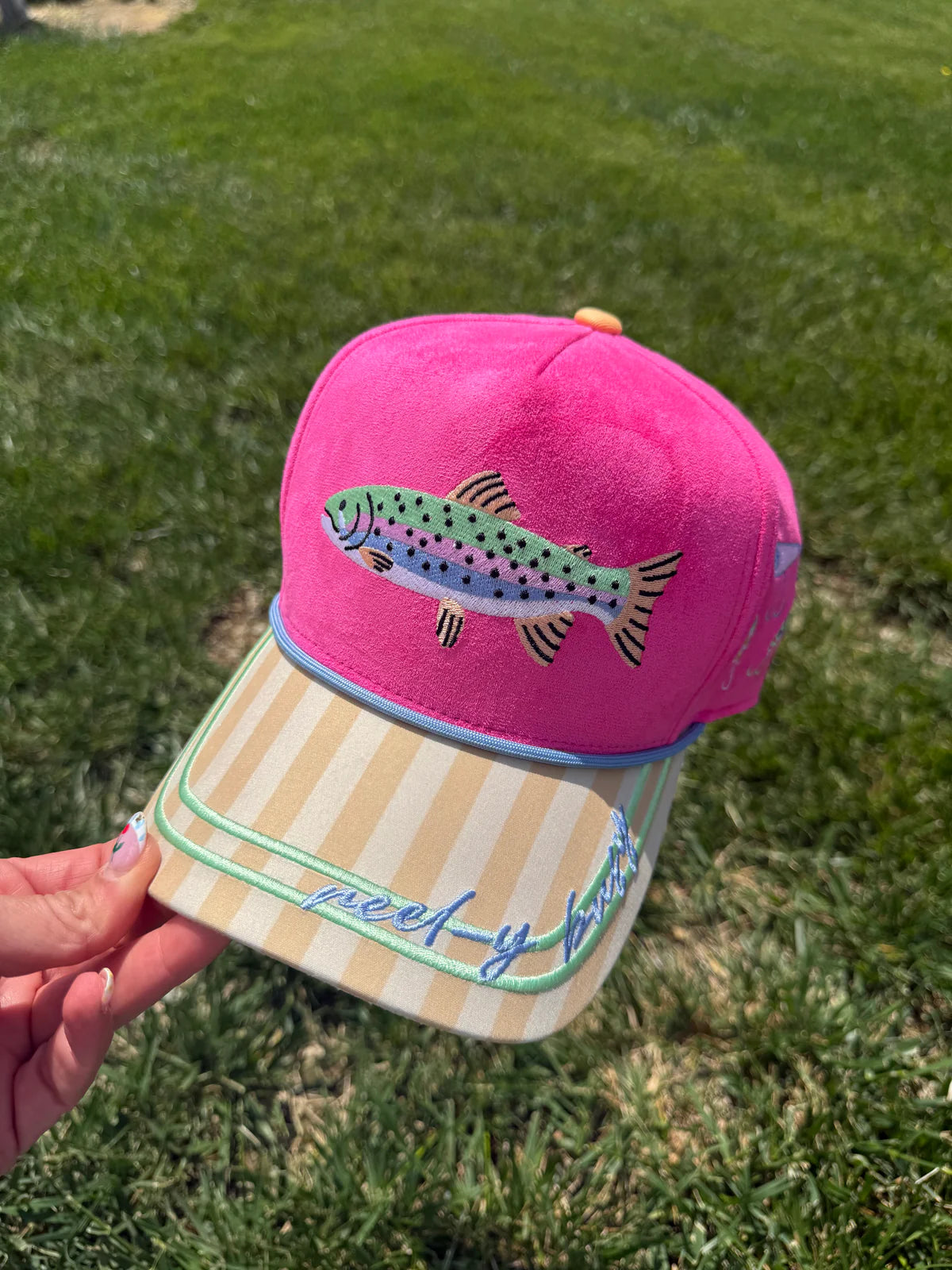 Pink faux suede and canvas snapback hat featuring an embroidered rainbow trout on the front, yellow striped brim with "Reel-y Busy" embroidery, periwinkle rope trim, fishing-themed side embroidery, and "Catch Ya Later" embroidered on the back.