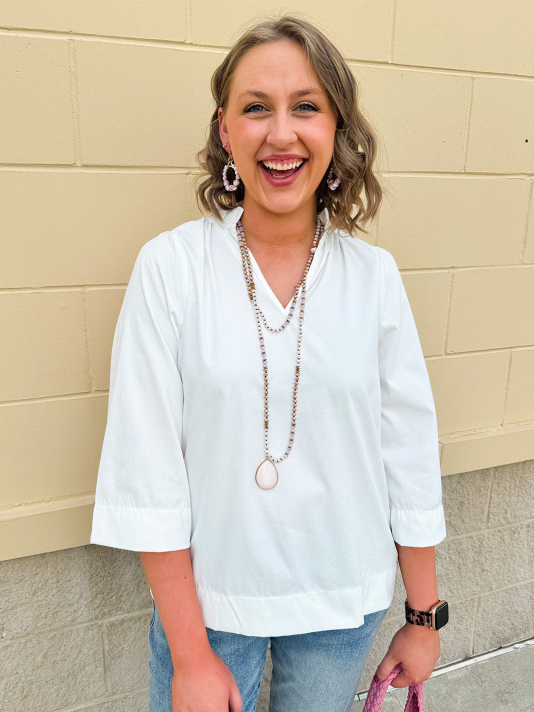 White blouse with ruffled V-neck and ¾ length wide sleeves, styled for a feminine, polished look.