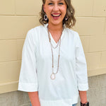White blouse with ruffled V-neck and ¾ length wide sleeves, styled for a feminine, polished look.