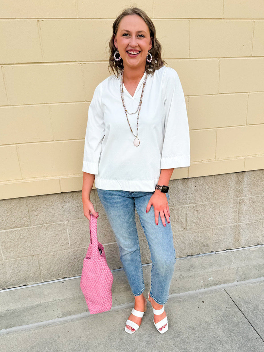 White blouse with ruffled V-neck and ¾ length wide sleeves, styled for a feminine, polished look.