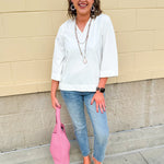 White blouse with ruffled V-neck and ¾ length wide sleeves, styled for a feminine, polished look.