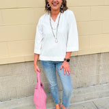 White blouse with ruffled V-neck and ¾ length wide sleeves, styled for a feminine, polished look.