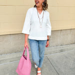 White blouse with ruffled V-neck and ¾ length wide sleeves, styled for a feminine, polished look.