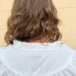 White blouse with ruffled V-neck and ¾ length wide sleeves, styled for a feminine, polished look.