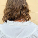 White blouse with ruffled V-neck and ¾ length wide sleeves, styled for a feminine, polished look.