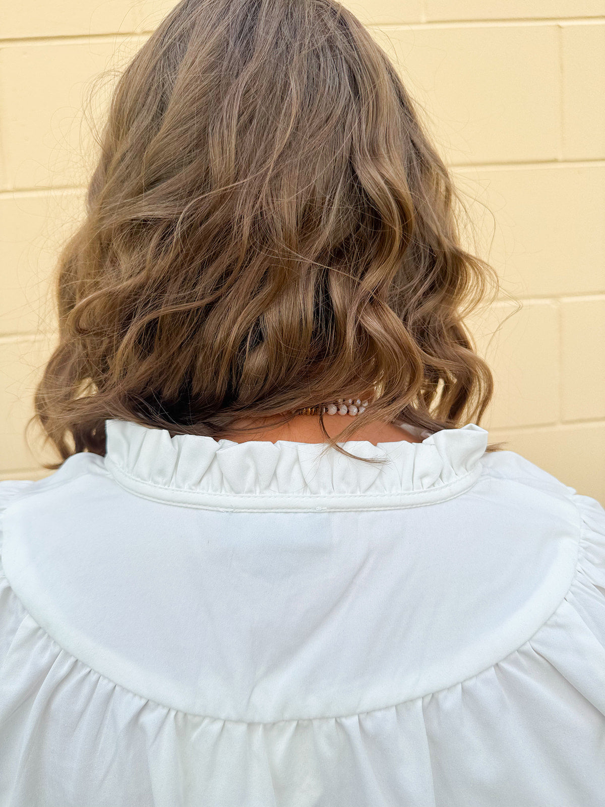 White blouse with ruffled V-neck and ¾ length wide sleeves, styled for a feminine, polished look.