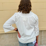 White blouse with ruffled V-neck and ¾ length wide sleeves, styled for a feminine, polished look.