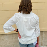 White blouse with ruffled V-neck and ¾ length wide sleeves, styled for a feminine, polished look.