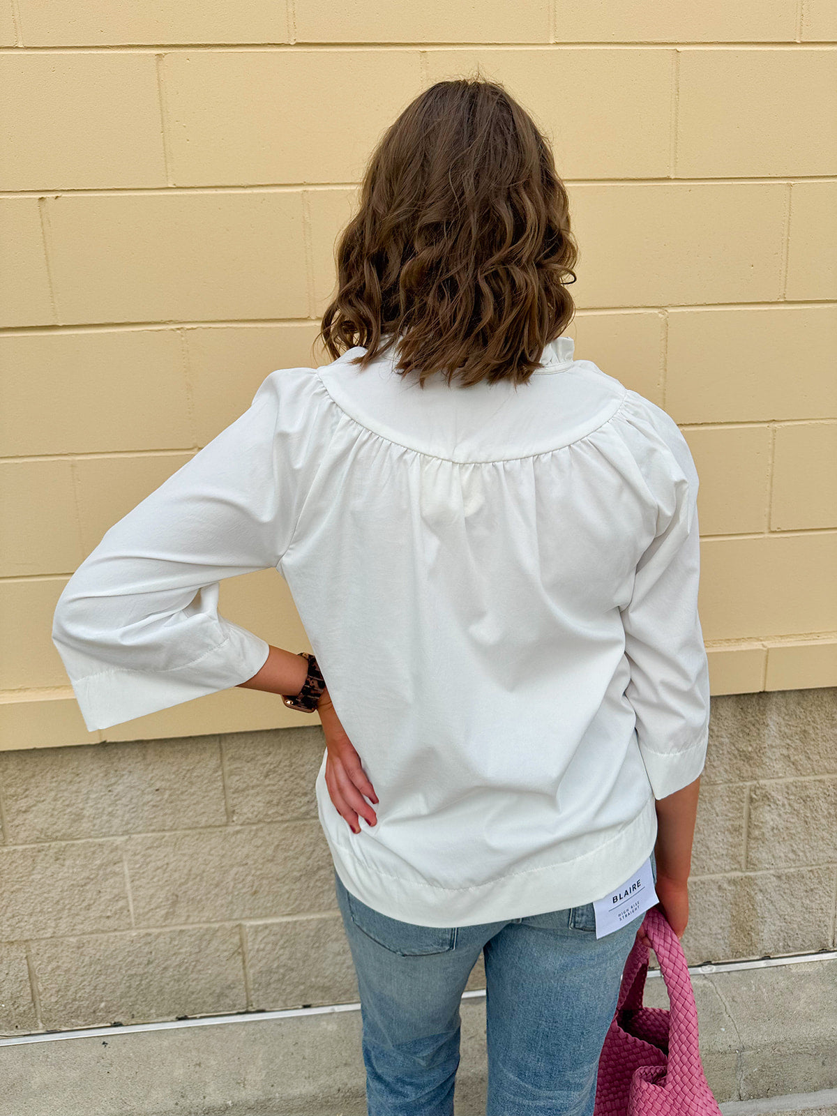 White blouse with ruffled V-neck and ¾ length wide sleeves, styled for a feminine, polished look.