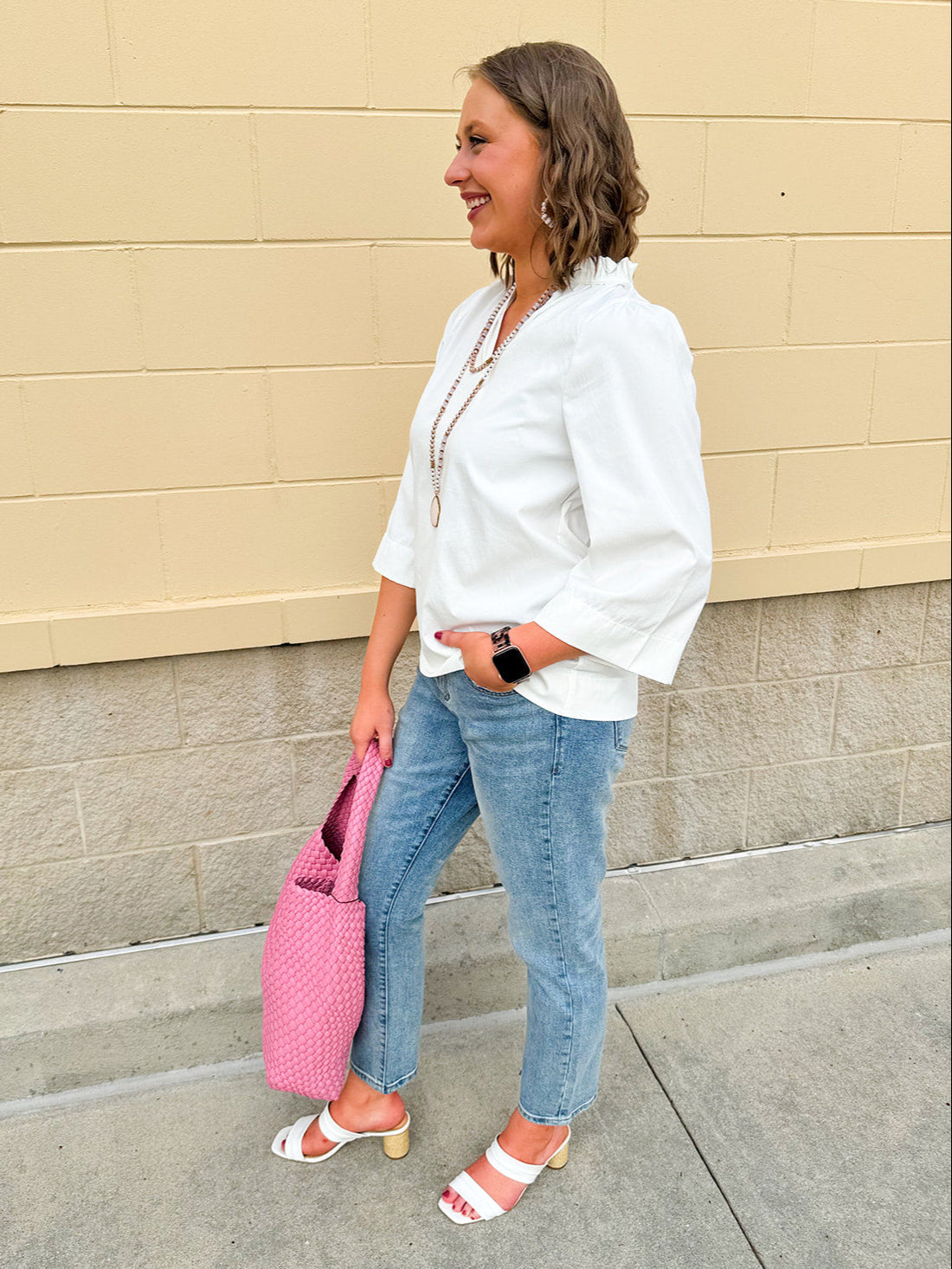 White blouse with ruffled V-neck and ¾ length wide sleeves, styled for a feminine, polished look.