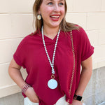 Garnet drop shoulder woven top with collared V-neckline, folded short sleeves, and center seam detail.