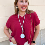 Garnet drop shoulder woven top with collared V-neckline, folded short sleeves, and center seam detail.