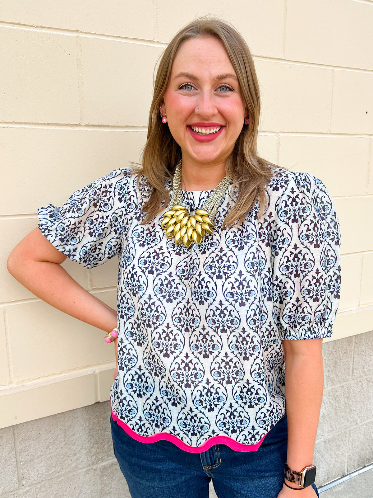 Women’s ivory top with navy and light blue porcelain-inspired print, short puff sleeves, gathered neckline, and hot pink scalloped hem trim.