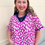 Hot pink and ivory abstract print women’s short sleeve top with navy contrast collar, V-neckline, and navy sleeve trim.