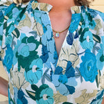 Blue floral blouse with pink accents, featuring a ruffle-trimmed split neckline and short puff sleeves