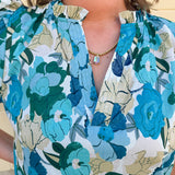 Blue floral blouse with pink accents, featuring a ruffle-trimmed split neckline and short puff sleeves