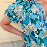 Blue floral blouse with pink accents, featuring a ruffle-trimmed split neckline and short puff sleeves