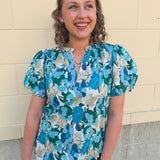 Blue floral blouse with pink accents, featuring a ruffle-trimmed split neckline and short puff sleeves