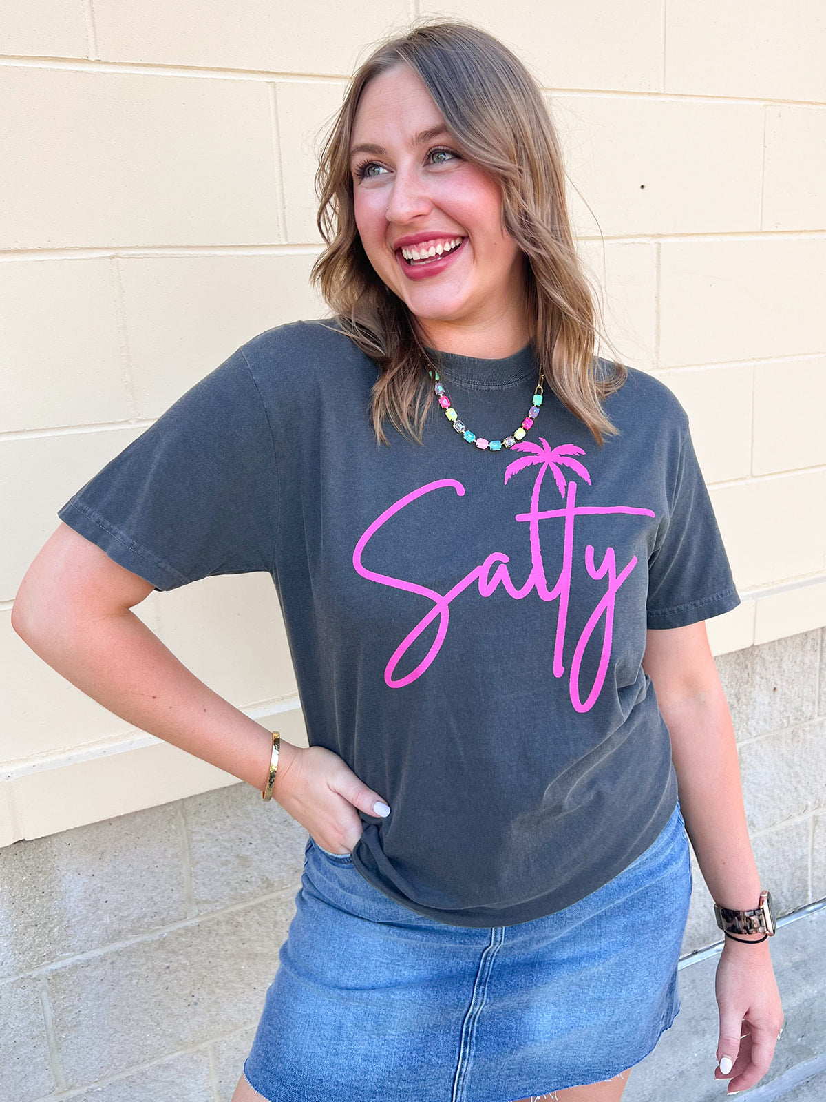 Charcoal gray graphic t-shirt featuring pink script "Salty" lettering with a palm tree graphic on the front.