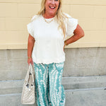 Lightweight printed wide-leg pants with a tropical pattern in dusty blue and cream tones, featuring a drawstring waist and pockets.