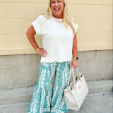 Lightweight printed wide-leg pants with a tropical pattern in dusty blue and cream tones, featuring a drawstring waist and pockets.