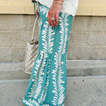 Lightweight printed wide-leg pants with a tropical pattern in dusty blue and cream tones, featuring a drawstring waist and pockets.